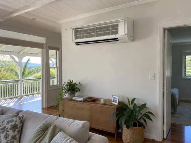 Clean split system head on a white living room wall above a timber cabinet in a modern home in Mudgeeraba