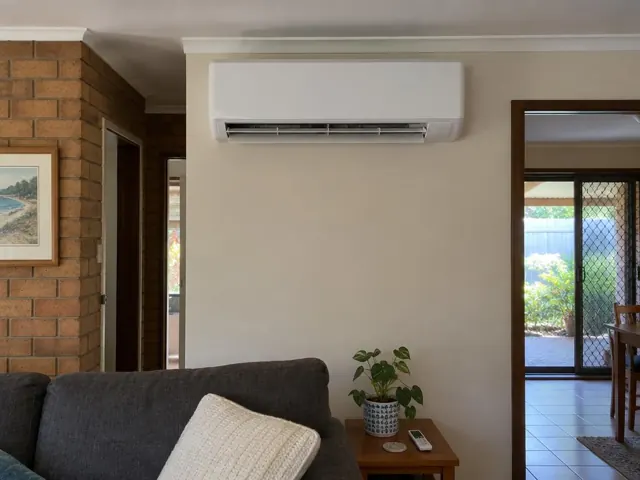 Clean split system indoor unit on a lounge room wall above a couch in a brick home in Nerang