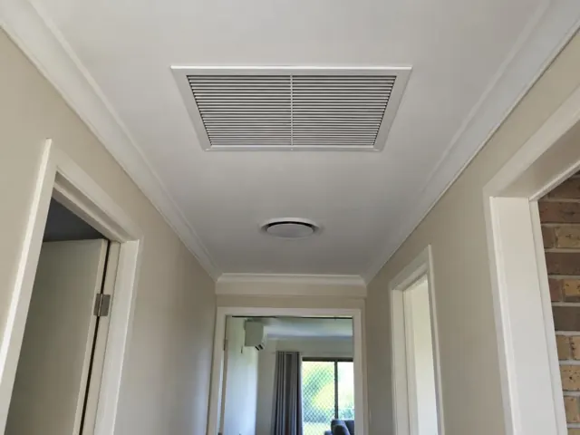 Ceiling return-air grille and round ceiling outlet in a hallway with white trim in Merrimac